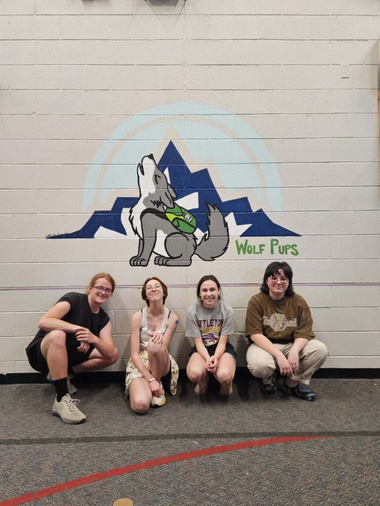 Vinny Anderson, Zora Young, Riley Irwin, and Zil Torres sitting Infront of their mural for a middle school.