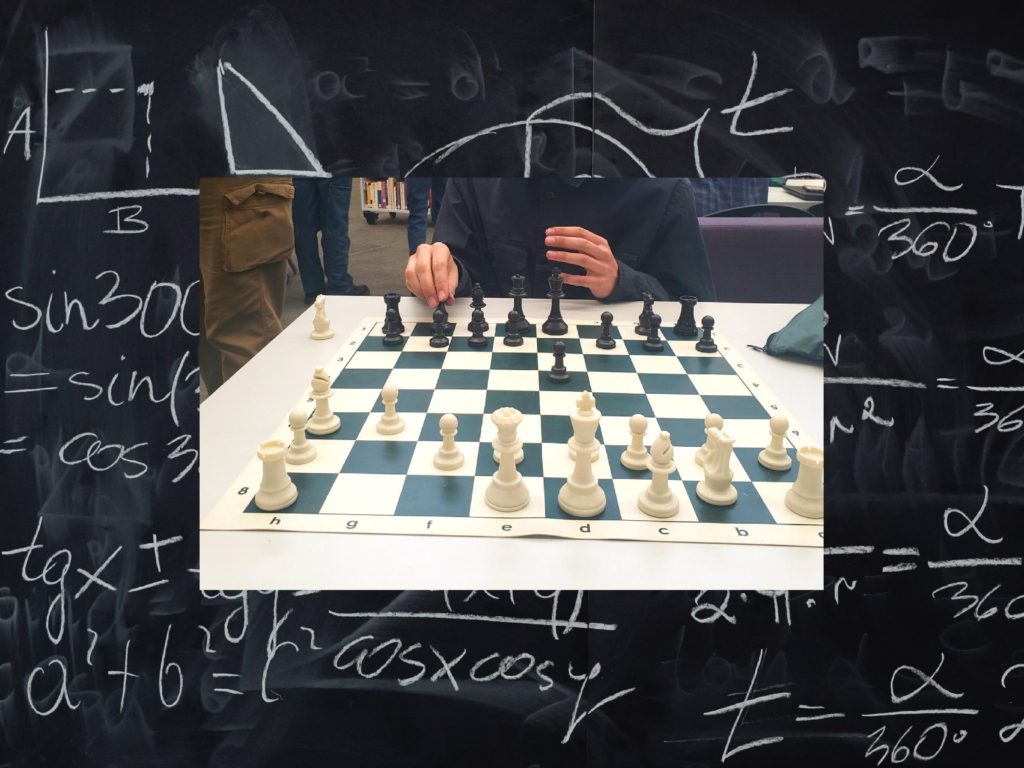 A chess board, mid-game, is pictured against a chalkboard with mathematical calculations drawn on it